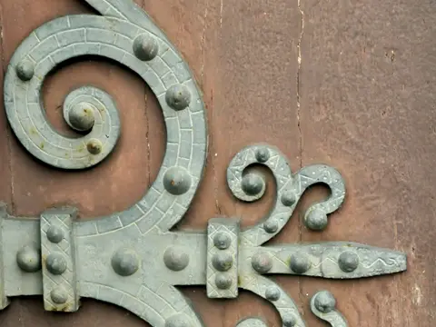 Grande penture de porte en métal vert-de-gris, à volutes et rivets, fixée sur une porte en bois