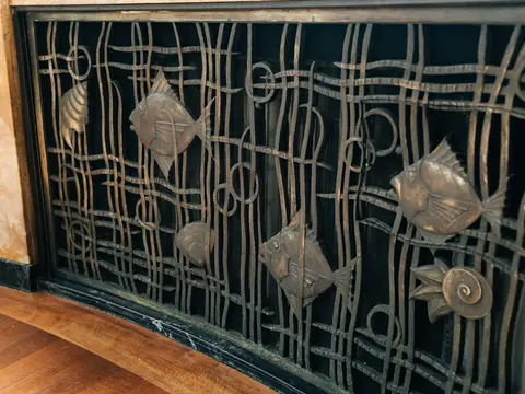Pare-feu Art déco en fer forgé aux barreaux martelés et entrelacés, orné de poissons et de coquillages en bronze, devant une cheminée de marbre