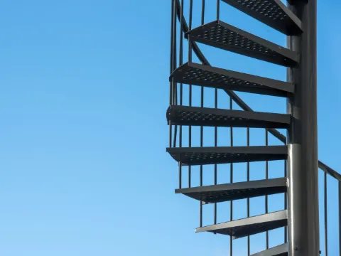 Escalier colimaçon en acier noir à marches ajourées se détachant sur un ciel bleu