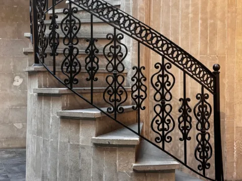 Escalier en colimaçon de pierre grise bordé d'une rampe en fer forgé noir à volutes