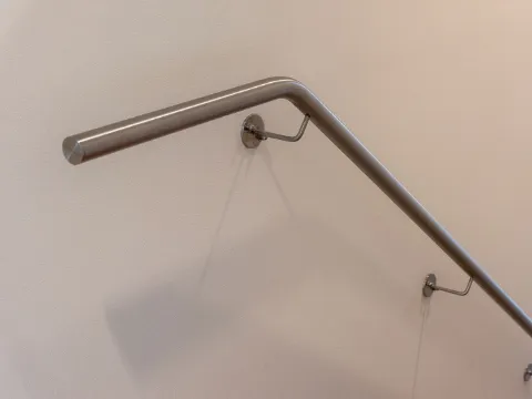 Main courante murale en inox brossé sur supports discrets le long d'un mur beige