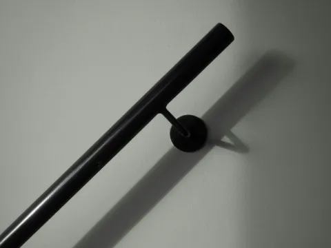 Main courante tubulaire noire fixée au mur par un support rond, avec son ombre portée