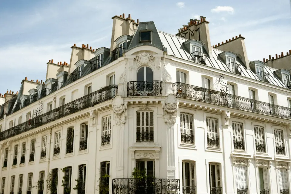 Façade blanche d'un immeuble haussmannien aux balcons en fer forgé noir sous un ciel bleu