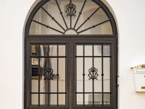 Haute porte cintrée à deux vantaux en fer noir et verre sur façade blanche