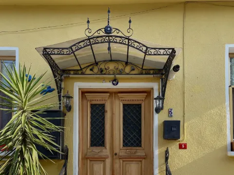 Auvent en fer forgé à volutes au-dessus d'une porte en bois sur une façade jaune, rampe d'escalier assortie