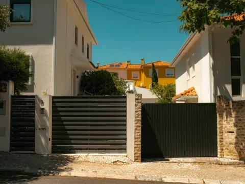 Portail à lames horizontales anthracite entre deux murs blancs d'une rue pavée ensoleillée