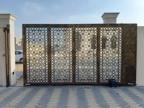 Grand portail coulissant en acier bronze découpé de motifs géométriques, vu de face sur des pavés